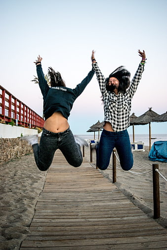 Two People Jumping Joyfully On Beach Boardwalk