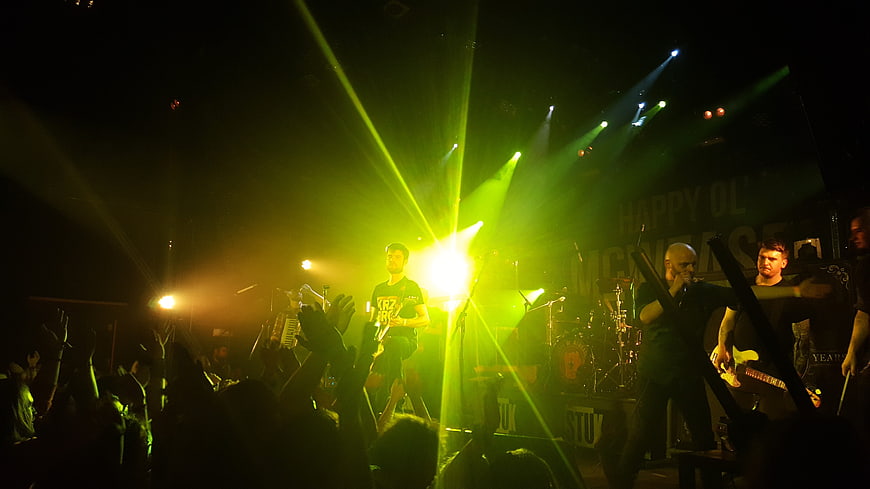 Live rock band performing on stage with green concert lighting and crowd