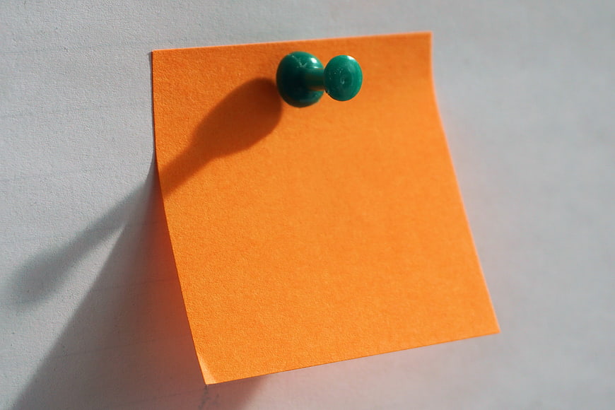Orange sticky note with green push pin on white background