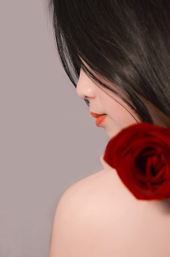 Close-up of woman with red rose on shoulder