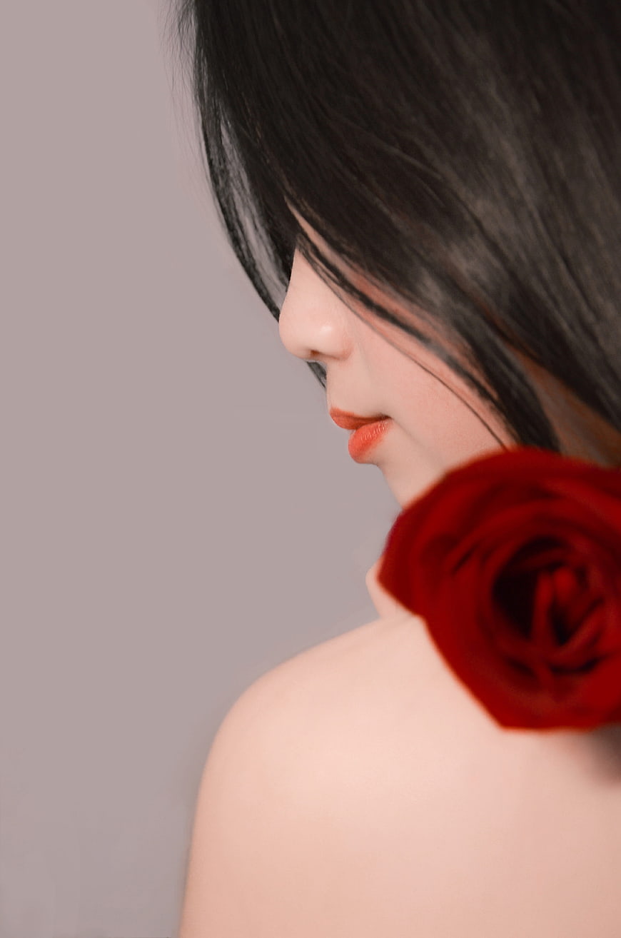 Close-up of woman with red rose on shoulder