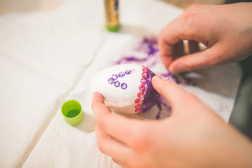 Close up of hands decorating Easter egg with glitter and gems