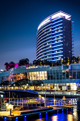 Modern illuminated hotel tower at night with marina and yacht
