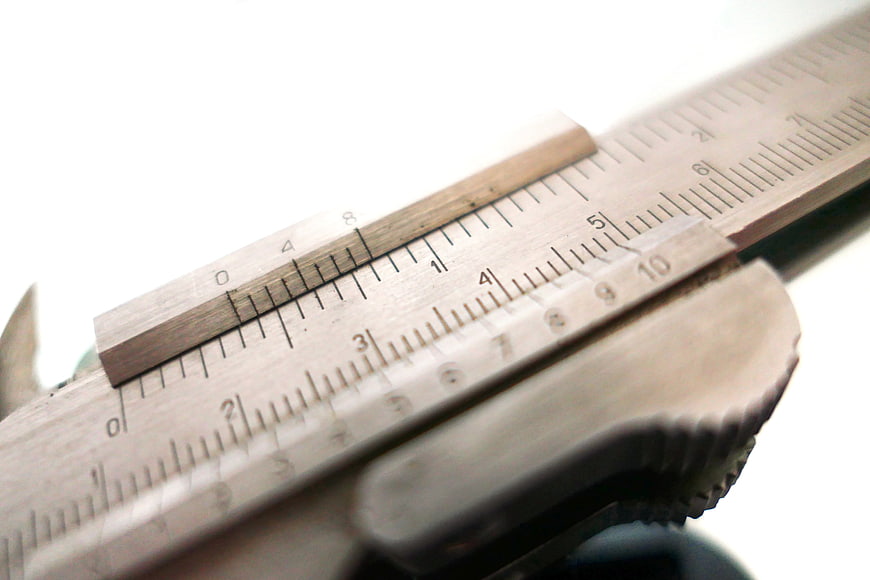 Close-up of metal calipers measuring a wooden piece