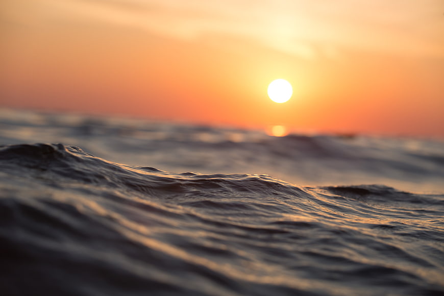 Close-up ocean waves at sunset with blurred sun background