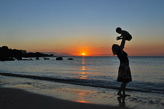 Mother Lifting Child Silhouette on Beach at Sunset