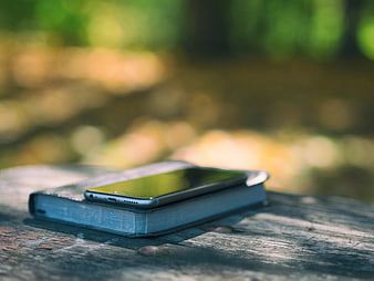 Smartphone resting on a book on a wooden table outdoors