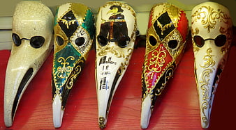 Five ornate Venetian plague doctor masks on red background