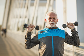 Senior man lifting dumbbells outdoors on bridge