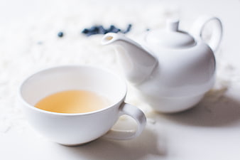 White teacup with rooibos tea and teapot on white background