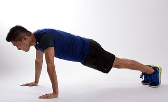 Man performing push-up in blue shirt on white studio background
