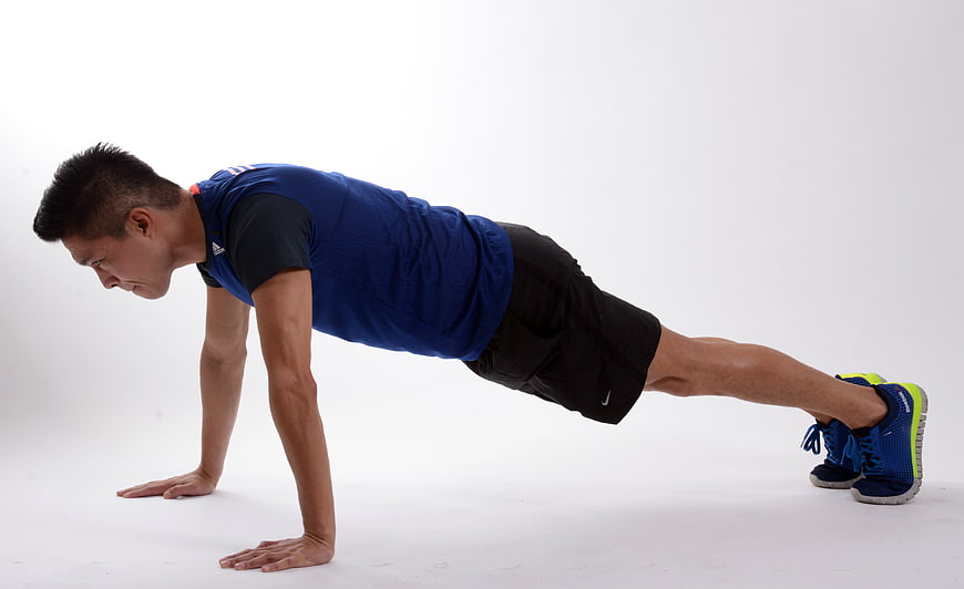 Man performing push-up in blue shirt on white studio background