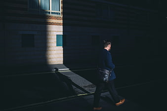 Man in Blue Blazer Walking in Shadowy Urban Street