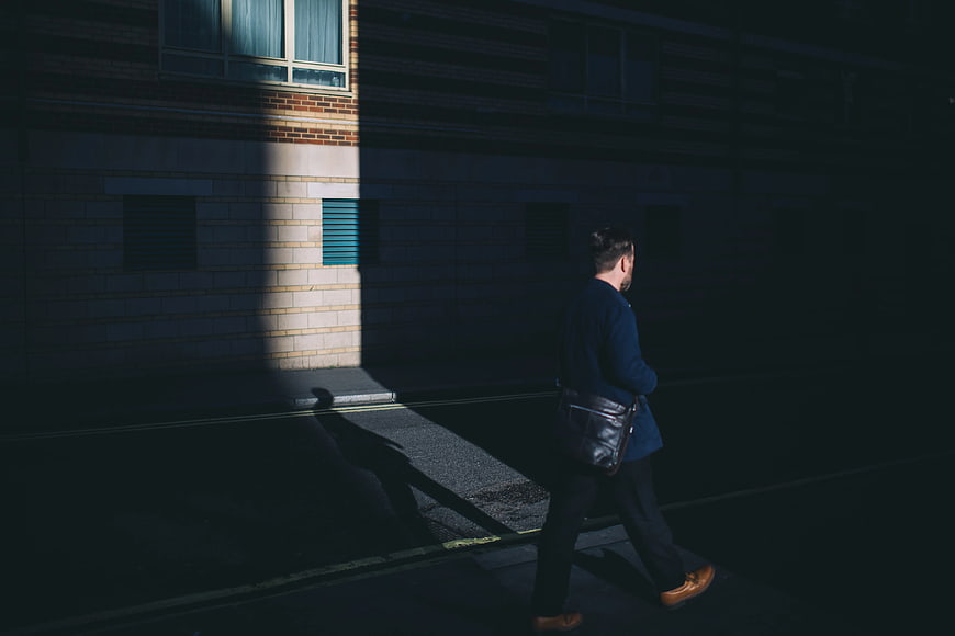 Man in Blue Blazer Walking in Shadowy Urban Street