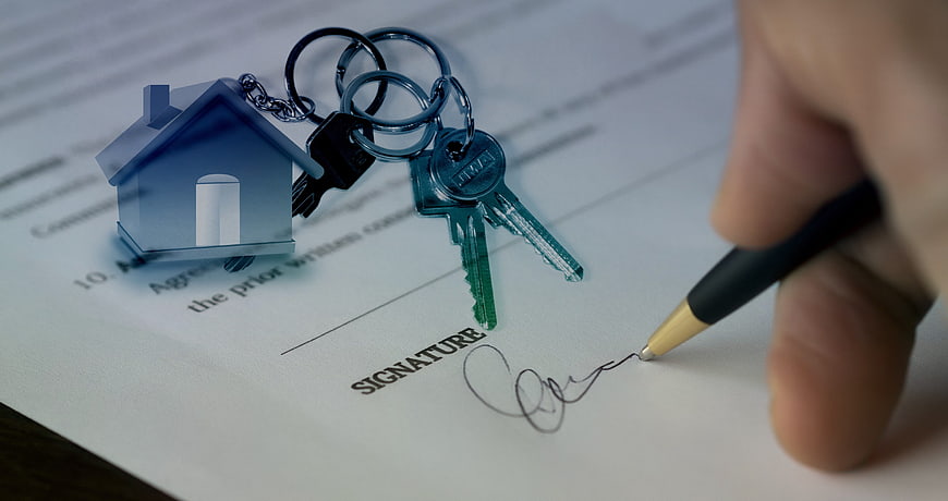 Hand signing real estate contract with house keychain and keys