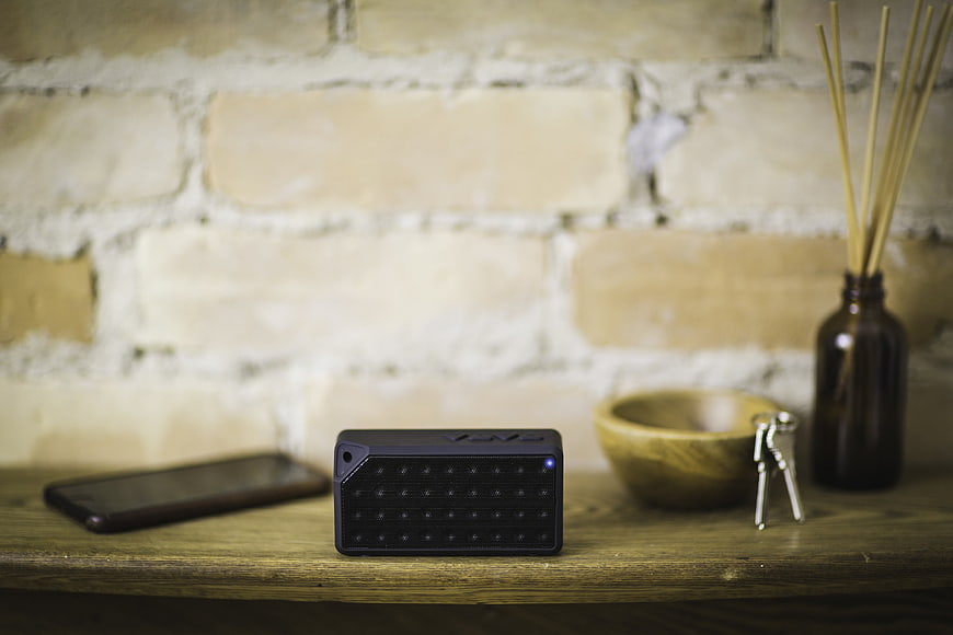 Black Bluetooth Speaker on Wooden Shelf with Smartphone and Keys