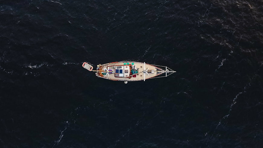 Aerial top-down view of sailboat on dark ocean