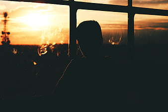 Silhouette of person looking out window at sunset