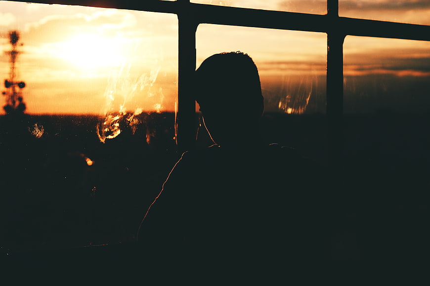 Silhouette of person looking out window at sunset