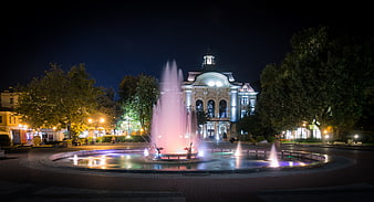 Illuminated fountain and historic building in city square at night
