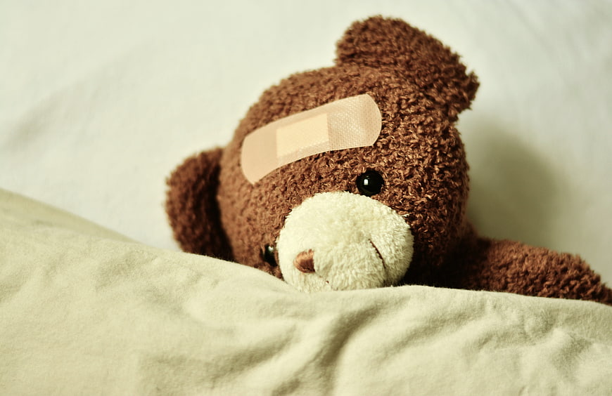 Sick Teddy Bear With Bandage On Bed