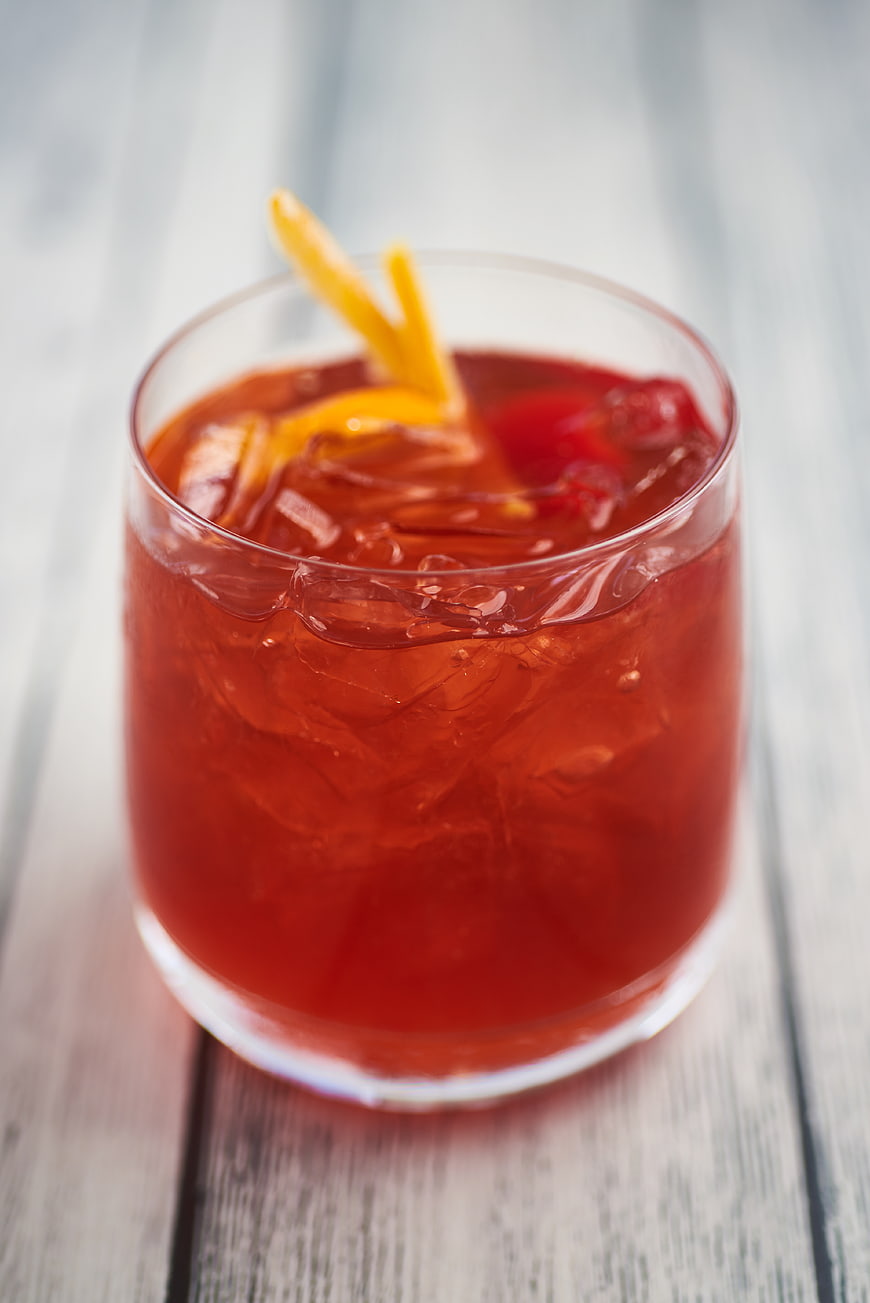 Refreshing Red Cocktail with Orange Twist and Cherry Garnish
