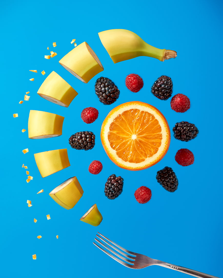 Fresh mixed fruit salad with banana, orange, and berries on blue background