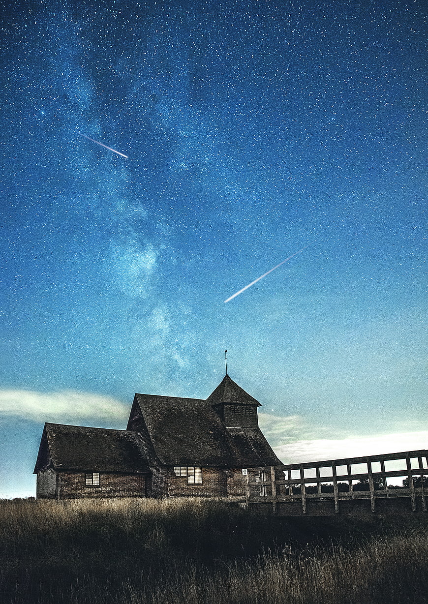 Rustic wooden church under starry night sky with shooting stars