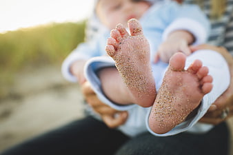 Close-up of baby feet covered in sand held by parent