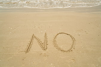 The word NO written in wet sand on a beach shoreline