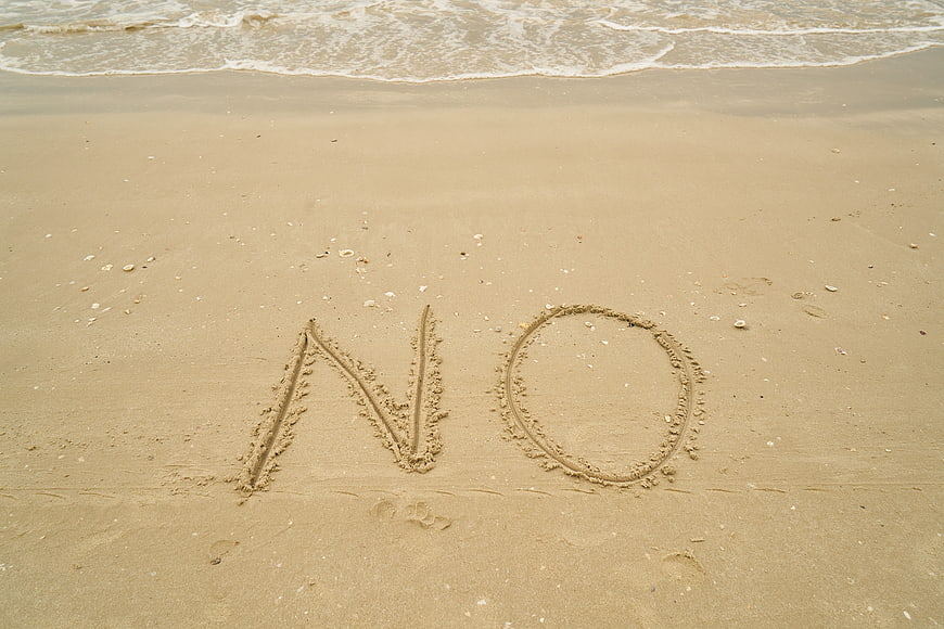 The word NO written in wet sand on a beach shoreline