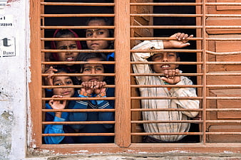 Children looking through wooden window bars in India