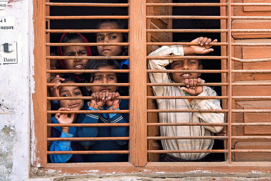 Children looking through wooden window bars in India