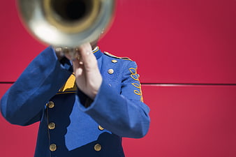 Marching band member playing trumpet against red wall