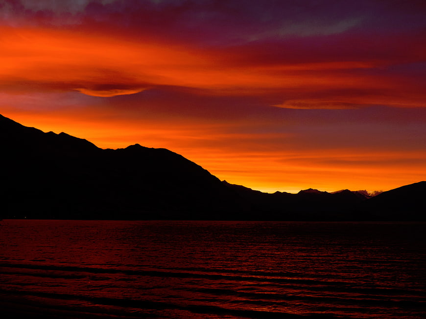 Dramatic fiery sunset over silhouetted mountains and water