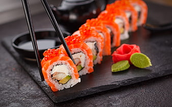 Salmon sushi rolls with roe and chopsticks on slate