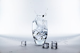 Glass of Water with Ice Cubes and Splash on White Background