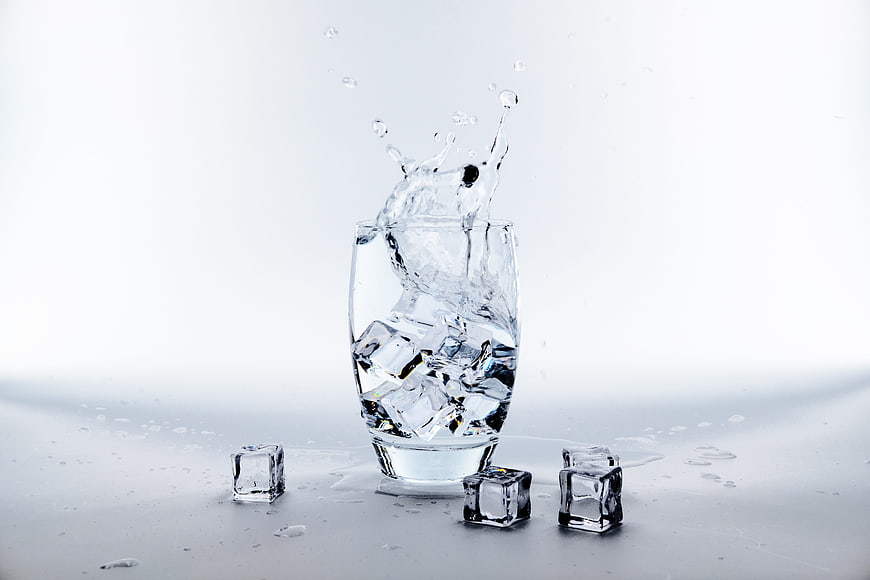 Glass of Water with Ice Cubes and Splash on White Background