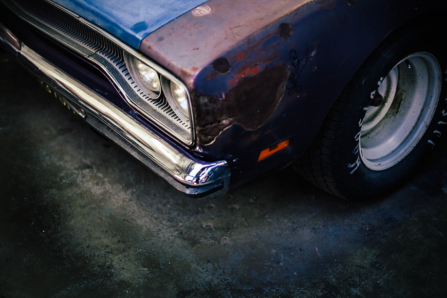 Close-up of vintage blue car with rust and chrome bumper