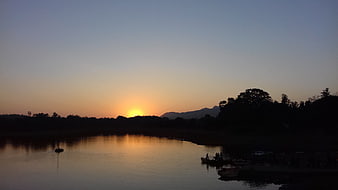 Serene Sunset Over River with Silhouetted Mountains and Boats