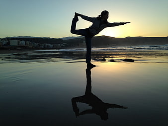 Woman performing yoga pose on wet beach at sunset