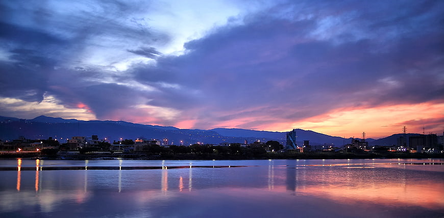 Dramatic sunset sky over river with city lights and mountains