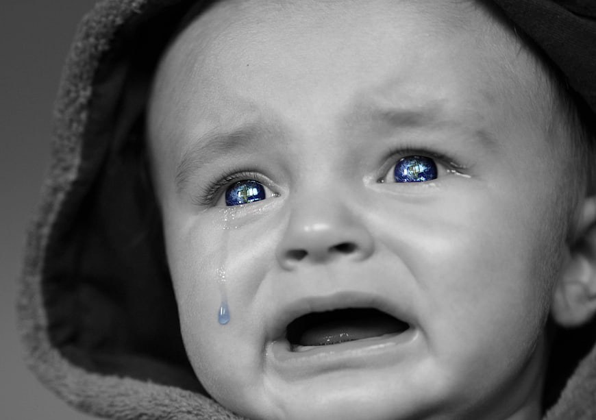 Close-up portrait of crying baby with blue eyes and tear