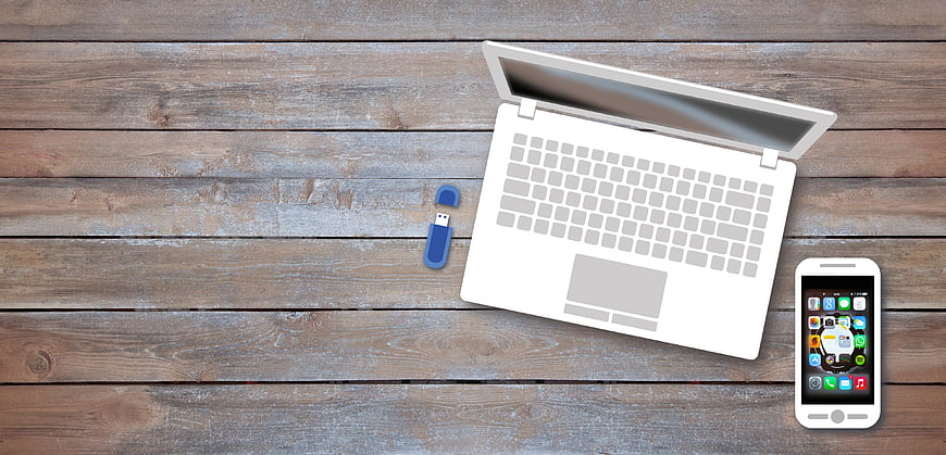 Flat lay of laptop, smartphone, and USB drive on wooden desk