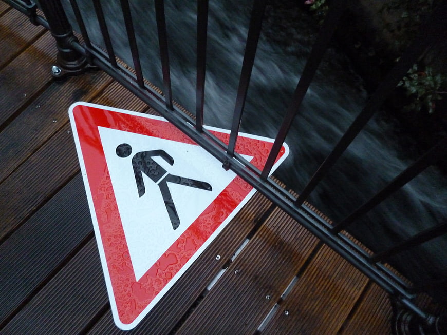 Wet pedestrian crossing sign on wooden bridge railing