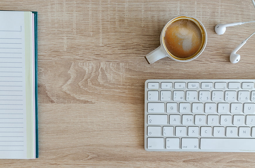 Flat lay workspace with coffee, keyboard, notebook, and earphones