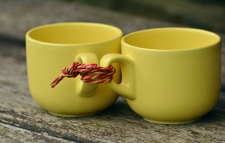 Two yellow ceramic mugs with handles tied together by a red and beige rope