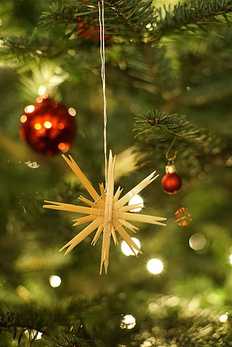 Handcrafted straw star ornament hanging on a Christmas tree with red baubles and warm lights