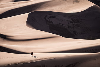 Two Hikers Walking on Massive Sand Dunes in Desert Landscape