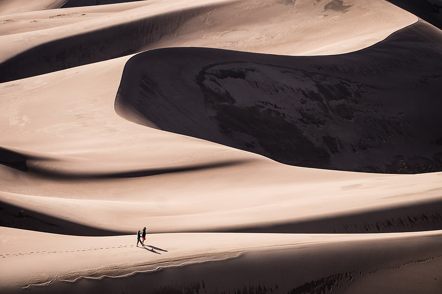 Two Hikers Walking on Massive Sand Dunes in Desert Landscape